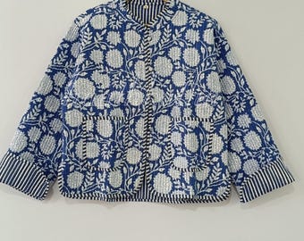 May include: A blue and white floral print jacket with a button-up front and two pockets. The jacket has a quilted design with a floral pattern and striped cuffs. The jacket is hanging on a wooden hanger.