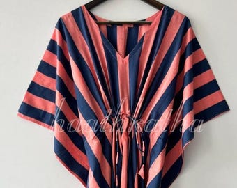 May include: A coral and navy striped kaftan dress with a V-neckline and drawstring waist. The dress features wide sleeves and a flowing silhouette. The fabric has a soft, lightweight appearance, suitable for warm weather. The dress is hanging on a wooden hanger.