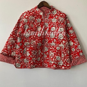 May include: A red quilted jacket with a floral pattern in white and grey. The jacket has a stand-up collar, two pockets, and striped cuffs. The text "haathkatha" is printed on the front.