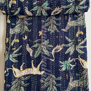 May include: A navy blue quilt with a jungle design. It features palm trees, leopards, zebras, and birds in green, yellow, and white. The quilt is hand-stitched with white thread.