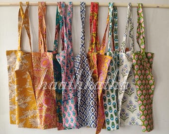 May include: A collection of eight fabric tote bags hanging in a row, each featuring distinct block-printed patterns in various colors including yellow, pink, blue, green, and white, with long shoulder straps and floral or geometric motifs.
