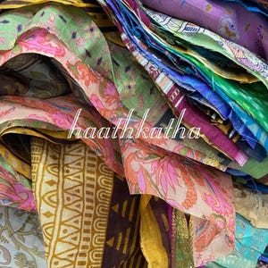 May include: A close-up of a pile of colorful fabric scraps. The fabrics feature a variety of patterns and colors, including pink, green, yellow, and purple. The text "haathkatha" is visible on the fabric.