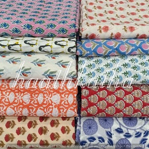 Może przedstawiać: Stos kolorowych tkanin z różnymi nadrukami. Wzory obejmują różowe i niebieskie ryby, pingwiny, motywy kwiatowe i geometryczne. Tkaniny są w odcieniach różu, bieli, pomarańczy, czerwieni i niebieskiego.