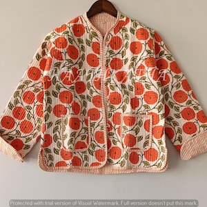 May include: A quilted jacket with a floral design. The jacket has a cream base with orange flowers and green leaves. It features two pockets and a striped trim. The jacket is displayed on a wooden hanger.