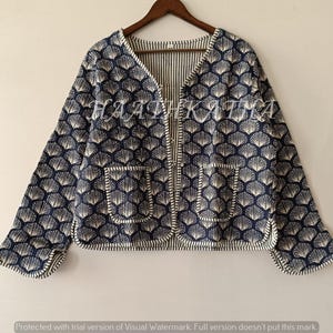 Op de afbeelding: Marineblauwe jas met een wit schelpenpatroon. De jas heeft lange mouwen, twee voorzakken en een gestreepte binnenvoering. De jas hangt aan een houten hanger.