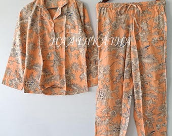 Op de afbeelding: Een oranje pyjamaset met een bloemenpatroon, bestaande uit een overhemd met knopen en een broek met trekkoord. De set heeft witte biezen en de tekst "HAATHKATHA". De stof heeft een zacht, bedrukt ontwerp.