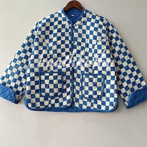 May include: A blue and white checked quilted jacket with a round collar and two front pockets. The jacket features a zip closure and solid blue cuffs and trim. The text "haathkatha" is visible on the jacket.