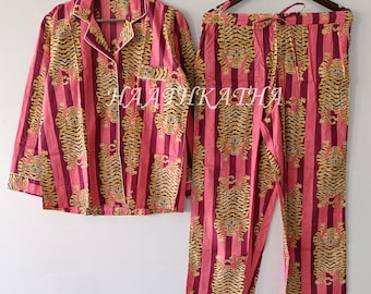 May include: Pink and gold striped pajama set with a tiger print. The set includes a button-down shirt with a chest pocket and pants with a drawstring waist. The text "HAATHKATHA" is visible on the shirt and pants.
