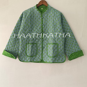 May include: A light blue quilted jacket featuring a repeating green circular pattern, a mandarin collar, and a front button closure. The garment includes two patch pockets, long sleeves with green cuffs, and the text HAATHKATHA printed across the front.