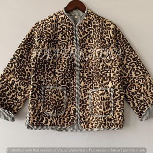 May include: A quilted jacket with a leopard print pattern in shades of brown and tan. The jacket has a mandarin collar, two front pockets, and striped cuffs. It is hanging on a wooden hanger.