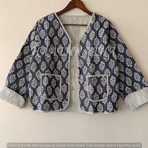 Puede incluir: Chaqueta acolchada azul marino con un estampado floral blanco. La chaqueta tiene cuello en V, dos bolsillos y puños a rayas. Cuelga de una percha de madera.