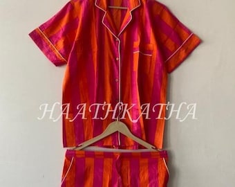 May include: A short-sleeve button-down shirt and matching shorts set featuring vertical stripes in vibrant orange and hot pink. The shirt has a notched collar, a single chest pocket, and white piping trim. The text HAATHKATHA is centered.