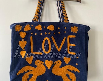 May include: Navy blue tote bag with embroidered orange details. The bag features the word "LOVE" and the text "hhathkatha" in orange, along with heart and bird designs. The handles have a striped pattern.