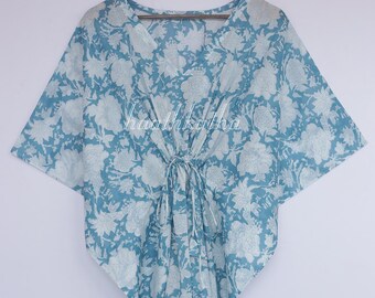 May include: A light blue caftan with a white floral pattern. The caftan has a V-neck and a drawstring at the waist. The fabric appears to be lightweight, and the sleeves are wide. The garment is hanging on a wooden hanger.