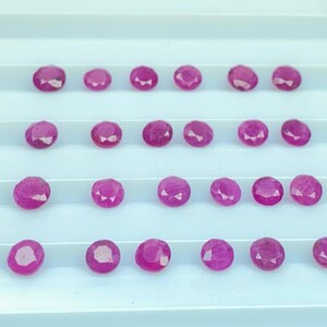 Könnte beinhalten: Eine Ansammlung oval geschliffener, leuchtend rosa Edelsteine, die in ordentlichen Reihen angeordnet sind. Die Edelsteine haben eine facettierte Oberfläche, die das Licht einfängt und eine satte, gesättigte Farbe zeigt. Die Steine liegen auf einer weißen Oberfläche.