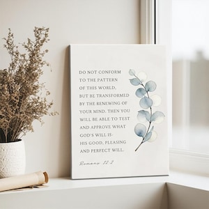 Könnte beinhalten: Weißer Leinwanddruck mit dem Text "DO NOT CONFORM TO THE PATTERN OF THIS WORLD..." und "Romans 12:2". Auf der rechten Seite befindet sich ein Aquarell-Eukalyptuszweig. Der Druck wird auf einer weißen Fensterbank angezeigt.