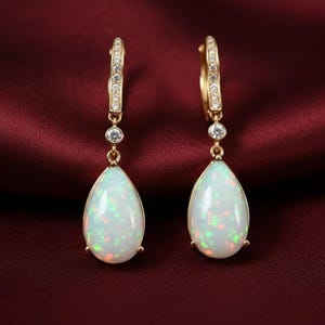 May include: A pair of gold-toned drop earrings featuring pear-shaped opals. The opals display a play of color with hints of green and orange. The earrings have a small diamond accent and a lever back closure.