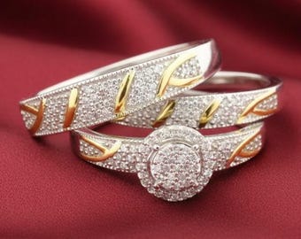 Könnte beinhalten: Drei silberne Ringe mit goldenen Akzenten und klaren Steinen. Die Ringe liegen auf einer roten Oberfläche. Der mittlere Ring hat einen runden Steinhaufen. Die anderen beiden Ringe haben ein ähnliches Design.