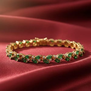May include: A gold bracelet with a repeating pattern of green emerald-cut stones and small white stones. The bracelet is set against a deep red satin background, creating a luxurious feel.
