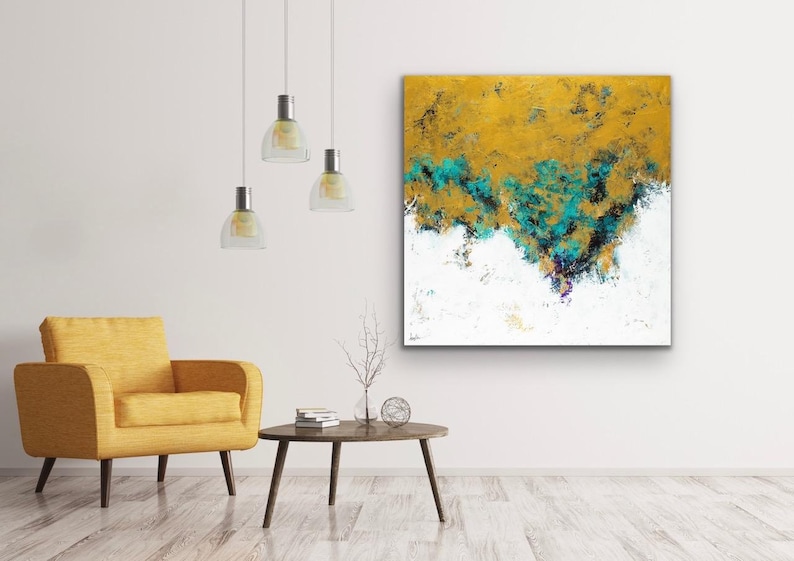 May include: Abstract art piece with a textured surface. The artwork features a blend of gold, teal, black, and white colors. The painting is displayed on a white wall above a yellow armchair and a small wooden table.