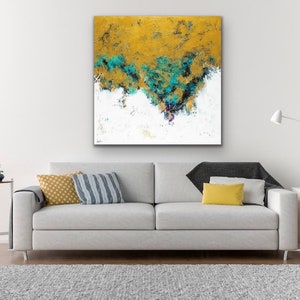May include: Abstract art canvas with a gold and teal color palette. The artwork features textured brushstrokes and a white base. The canvas is displayed above a gray sofa with decorative pillows and a rug.