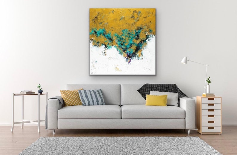 May include: Abstract art canvas with a gold and teal color palette. The artwork features textured brushstrokes and a white base. The canvas is displayed above a gray sofa with decorative pillows and a rug.