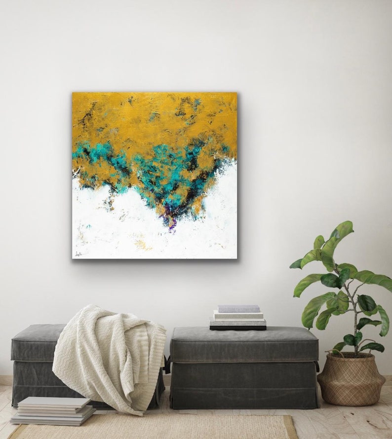 May include: Abstract art painting with a gold, teal, and white color palette. The artwork features textured brushstrokes and a layered composition. The painting is displayed on a white wall above two gray ottomans, a blanket, and a plant in a woven basket.