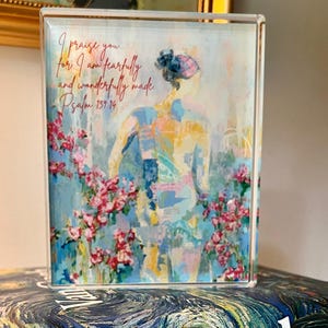 May include: A rectangular acrylic block featuring an artistic depiction of a figure with floral accents and the text "I praise you... for I am fearfully and wonderfully made. Psalm 139:14." The artwork is in shades of blue, pink, and yellow.