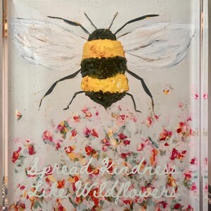 May include: A square, clear glass block with a painted bee and floral design. The bee is yellow and black with white wings. The text "Spread Kindness Like Wildflowers" is written in white script across the bottom.