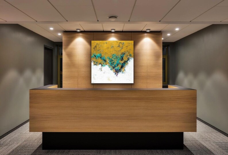 May include: A modern reception desk with a square abstract painting. The painting features gold, teal, and white colors. The desk is made of wood and has a black base. The room has recessed lighting and gray walls.