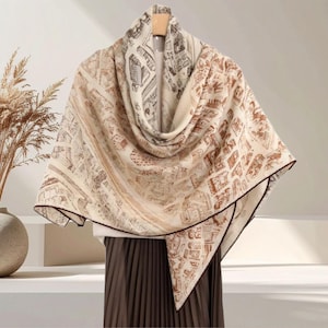 May include: A beige and brown scarf with a city map design. The scarf is draped over a hanger, showcasing its rectangular shape and dark brown trim. The scarf's pattern features detailed architectural elements.