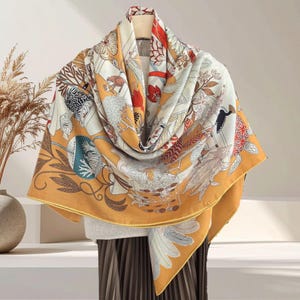 May include: A large square scarf featuring a vibrant mustard yellow border and a central cream-colored field. The fabric is decorated with intricate illustrations of stylized birds, fish, botanical elements, and geometric patterns in red, black, and white.