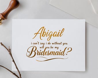 May include: A white rectangular card featuring gold foil text that reads Abigail, i can't say i do without you. will you be my Bridesmaid? The card is accompanied by a wooden wax seal stamp and a white envelope, creating a formal stationery set.