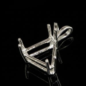 Könnte beinhalten: Eine silberfarbene Anhängerfassung mit dreieckigem Design. Die Fassung hat vier Krappen und eine Schlaufe für eine Kette. Das Metall reflektiert das Licht und erzeugt Glanzlichter und Schatten vor dem schwarzen Hintergrund. Diese Schmuckkomponente ist für einen Edelstein bestimmt.