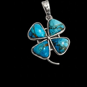May include: A silver pendant shaped like a four-leaf clover. Each leaf features a turquoise stone with brown veining. The pendant has a silver bail for a necklace. The pendant is approximately 3 cm in length.