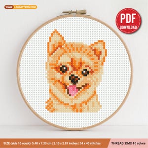 Puede incluir: Un patrón de punto de cruz de un perro Pomerania en un bastidor de bordado de madera. El perro está representado en tonos de naranja, beige y marrón, con una lengua rosa. El patrón mide 5,40 x 7,30 cm y utiliza 10 colores de hilo DMC.