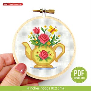 以下が含まれることがあります： 10.2 cmの木製フレームに入ったクロスステッチ刺繍。ピンクのバラ、黄色の花、黄色の蝶が描かれた黄色のティーポットが特徴です。「PDF DOWNLOAD」の文字が見えます。
