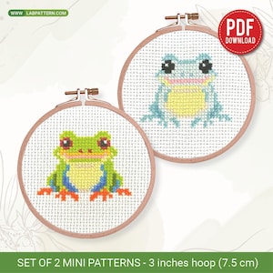Könnte beinhalten: Zwei Kreuzstichmuster von Fröschen in Holzreifen. Ein Frosch ist grün, blau und gelb, der andere blau und gelb. Die Reifen haben einen Durchmesser von 7,5 cm. Der Text "PDF DOWNLOAD" ist enthalten.