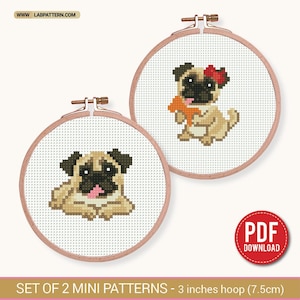 May include: Two circular wooden embroidery hoops containing cross-stitch patterns of tan pugs with black faces. One pug wears a red bow and holds an orange star, while the other lies down with a pink tongue visible. Text reads WWW.LABPATTERN.COM.