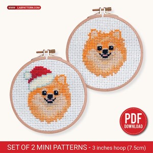 Puede incluir: Dos mini patrones de punto de cruz de perros Pomerania en aros de madera, cada uno de 7,5 cm de diámetro. Un perro lleva un gorro de Papá Noel. Los perros son de color naranja y blanco, con ojos y nariz negros. El texto "WWW LABPATTERN.COM" está en la parte superior.