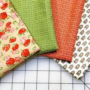Peut inclure: Quatre échantillons de tissu aux motifs et couleurs variés. L'un présente un motif floral avec des roses rouges et roses sur fond crème. Les autres comprennent du vert, de l'orange et un tissu blanc avec des motifs de maisons brunes.