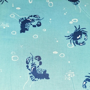 May include: Light blue fabric with a repeating pattern of dark blue crabs and lobsters, along with white bubbles and small clusters of white dots. The design has a nautical theme.