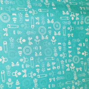 May include: Turquoise fabric with a repeating pattern of white baby-themed icons. The design includes buttons, pacifiers, safety pins, bows, and rattles. This fabric is suitable for baby-related crafts and projects.