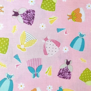 May include: Pink fabric with a repeating pattern of cartoon dresses in various colors, including yellow, green, blue, and purple. The dresses have different designs and are interspersed with white daisy flowers and small yellow and blue decorative elements.