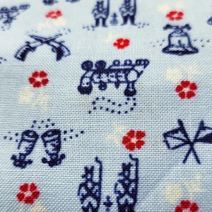 May include: Pale blue fabric featuring a repeating pattern of navy blue figures, crossed rifles, and red floral accents. The design includes bell shapes and other stylized elements, creating a vintage aesthetic.