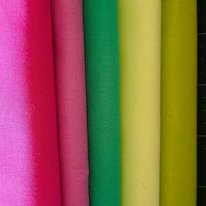May include: A collection of colorful fabric rolls in shades of pink, green, and yellow. The rolls are tightly wound, showcasing the texture and vibrant hues of the material. The colors range from bright fuchsia to a soft lime green.