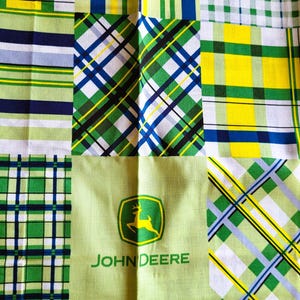 May include: A patchwork fabric with a variety of plaid and checkered patterns in green, yellow, blue, and white. The center square features the John Deere logo with a green background and the text "JOHN DEERE".