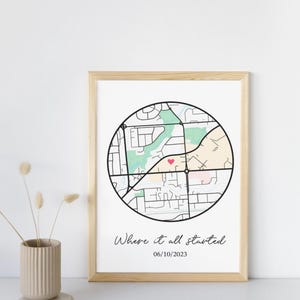 May include: A framed print featuring a circular map design with a heart-shaped marker. The map is in black and white, with green and pink accents. The text "Where it all started" and the date 06/10/2023 are below the map. The frame is light wood.