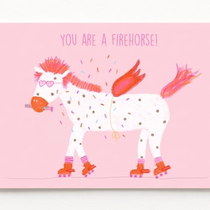 Peut inclure: Carte de vœux rose avec le texte "YOU ARE A FIREHORSE!". L'illustration représente un cheval blanc avec des accents roses et oranges, des patins à roulettes et une barre chocolatée dans la bouche. Le cheval a des ailes et est couvert de vermicelles.