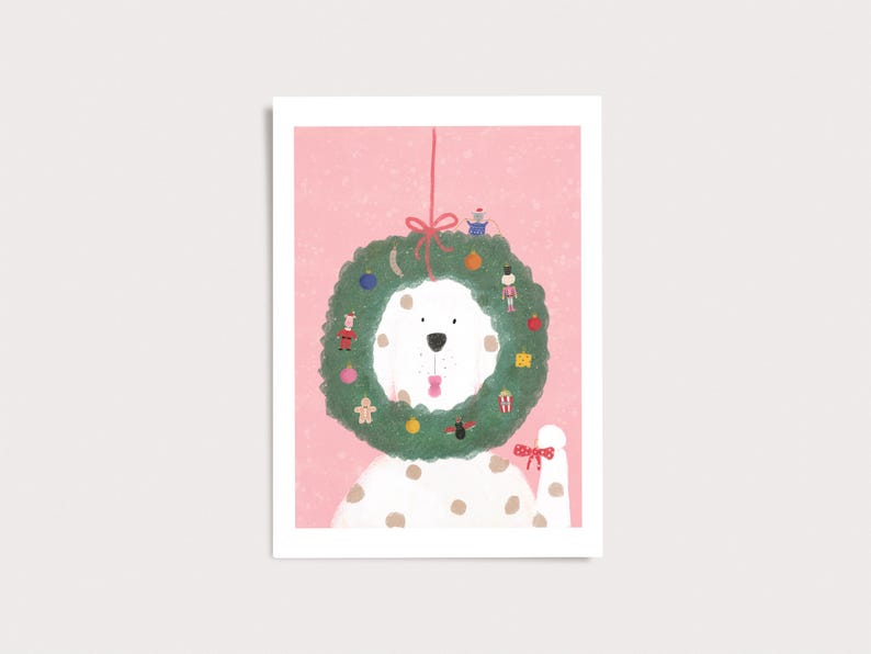 Peut inclure: Un chien blanc &agrave; taches brunes portant une couronne de No&euml;l verte autour du cou sur un fond rose. La couronne est d&eacute;cor&eacute;e de petits ornements, dont un casse-noisette, un bonhomme en pain d'&eacute;pices et des cadeaux, nou&eacute;e par un ruban rouge.